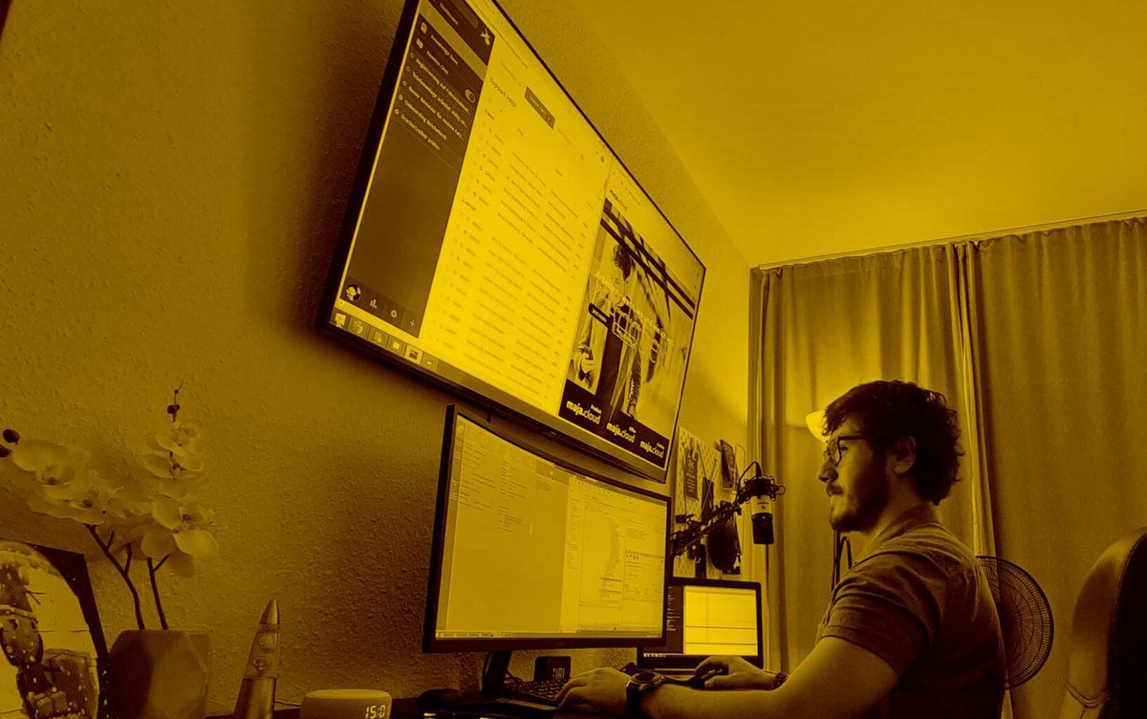 Junger Mann arbeitet am Schreibtisch vor einem großen Bildschirm